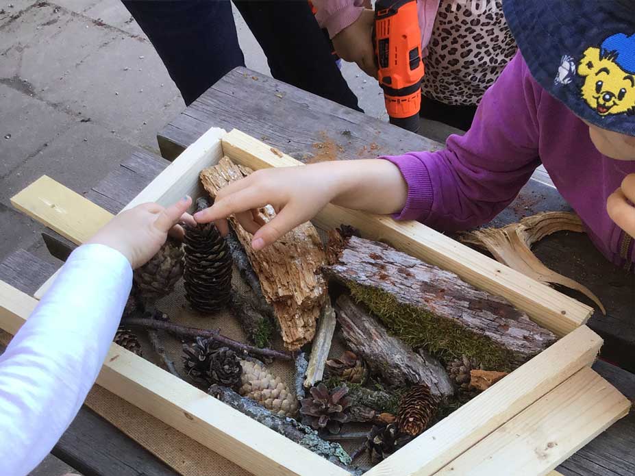 Barn lägger naturmaterial i en låda som ska bli ett bihotell